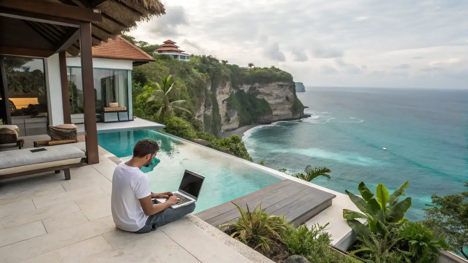 A resident working on a laptop beside a clifftop pool above the ocean.